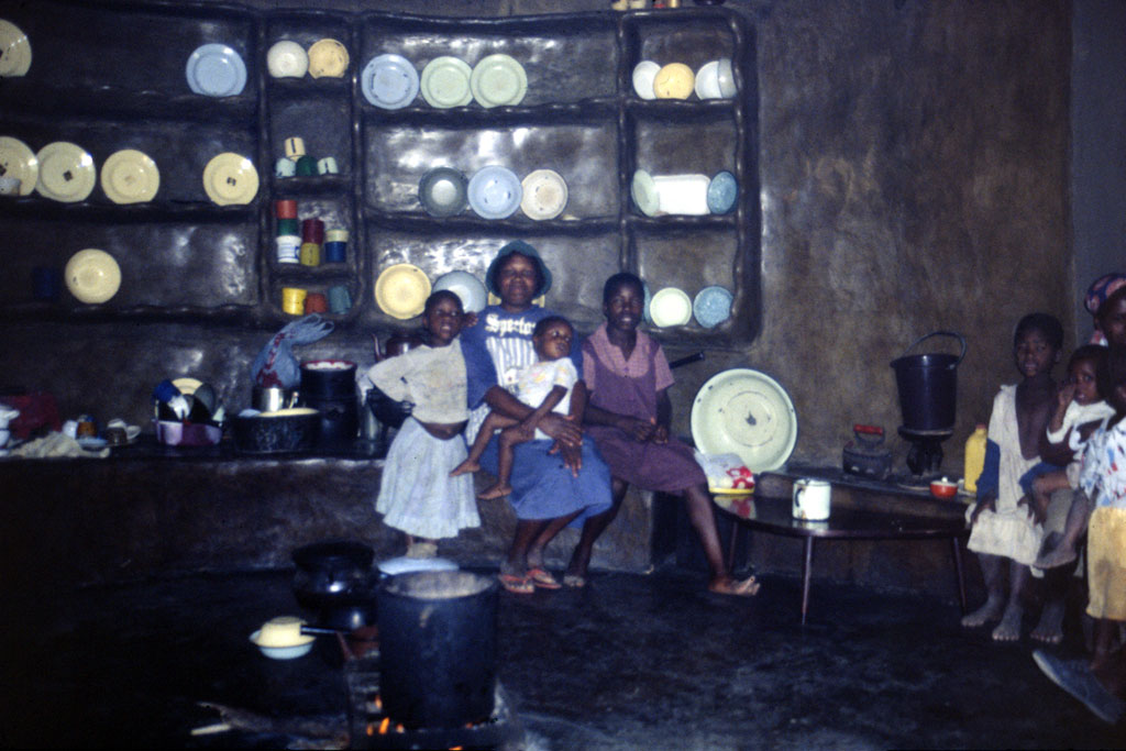 Women and children around the fireplace in a hut