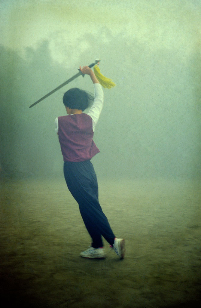 Ung kvinde laver tai qi med sværd en tåget morgen i en park i Chengdu