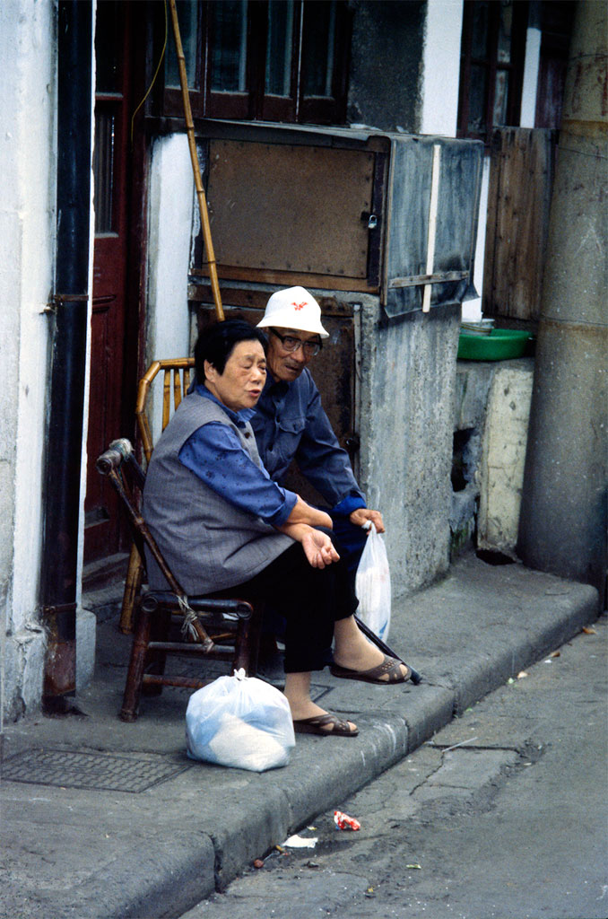 To ældre sidder ved fortorvet og sludrer om dagligdagen i Shanghai