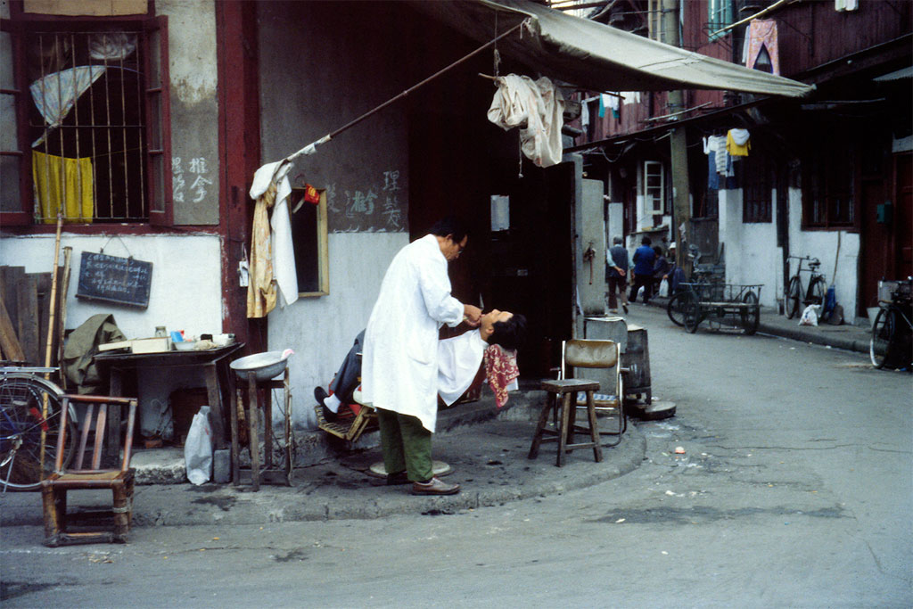 Shanghai - The barber shaving his customer on the sidewalk in a quiet street