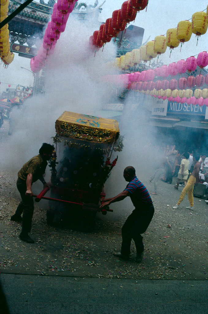 A sedan chair with religious figures is carried through the firecrackers